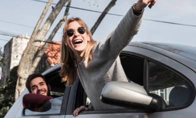 Two people hanging out of the window of a parked car and pointing into the distance