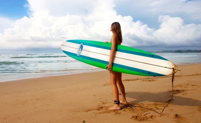 Female surfer standing on a beach, holding a surfboard, looking out to sea