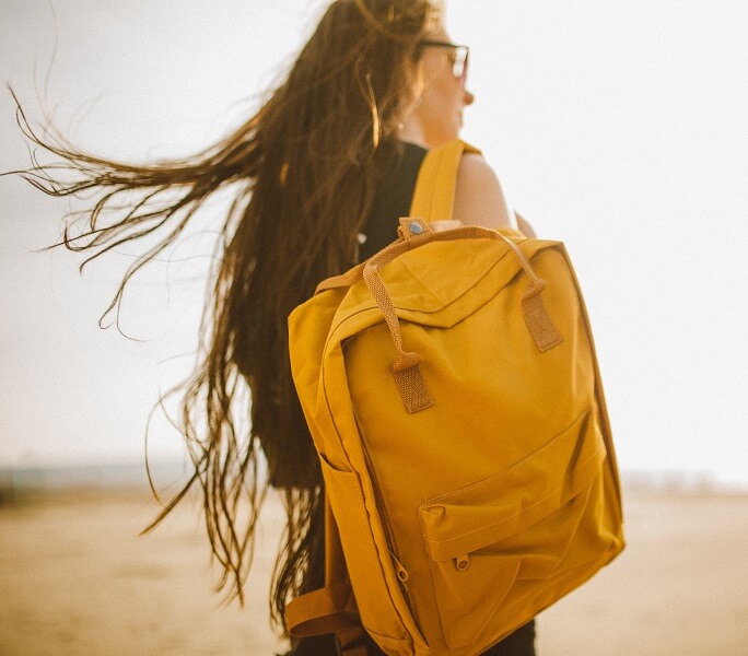Woman wearing glasses, holding a yellow backpack over her right shoulder, looking to her right