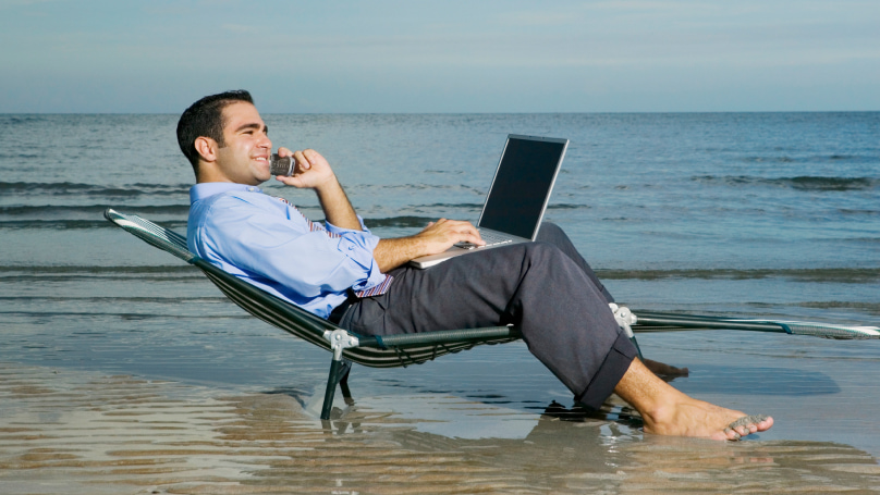 man sitting on the beach with his laptop