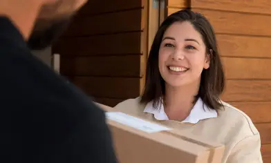 A delivery person hands a package to a smiling homeowner outside an open front door.