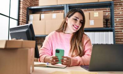 a smiling person surrounded by parcels with a smartphone and laptop