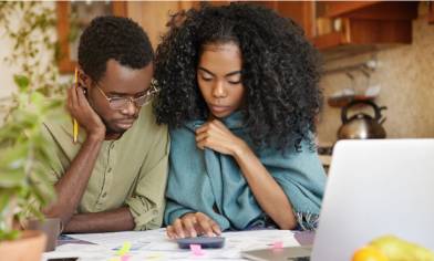 Two people looking at bills on a kitchen table with a laptop, calculator and various documents