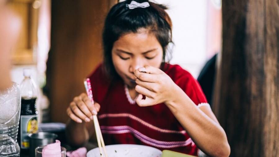 Woman sitting in a restaurant holding chopsticks eating soup