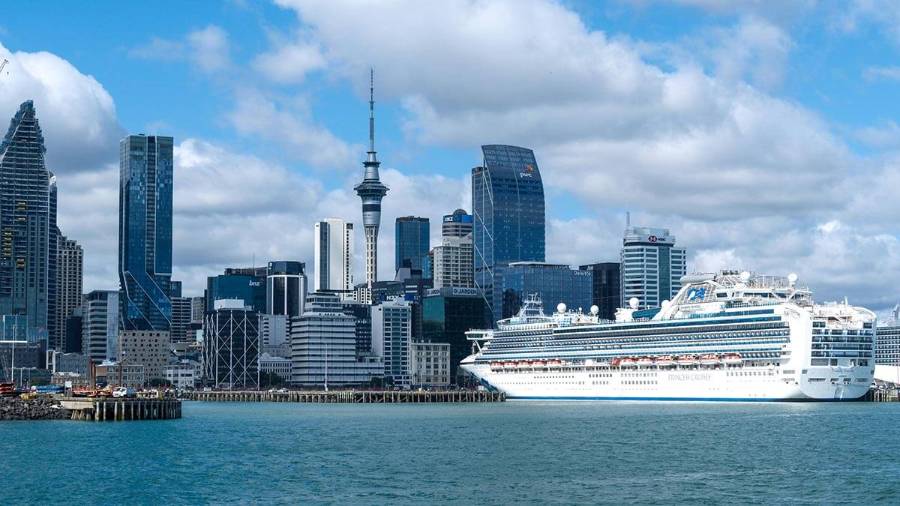 A cruise ship is docked by a modern city skyline under a partly cloudy sky