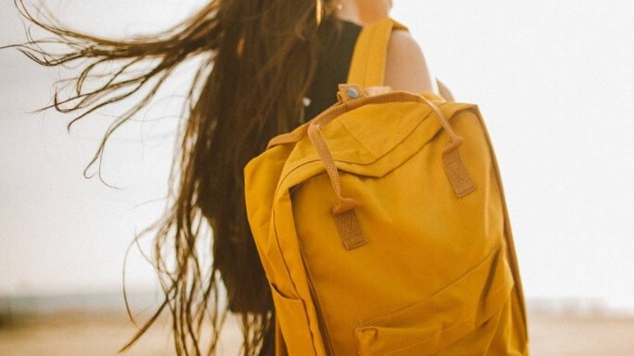 Woman wearing glasses, holding a yellow backpack over her right shoulder, looking to her right
