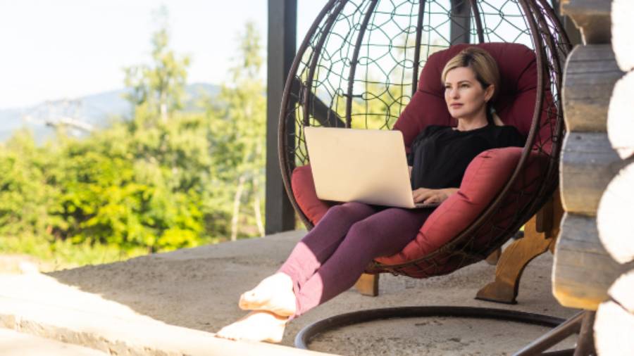 a person with a laptop lounging in a wicker chair outdoors