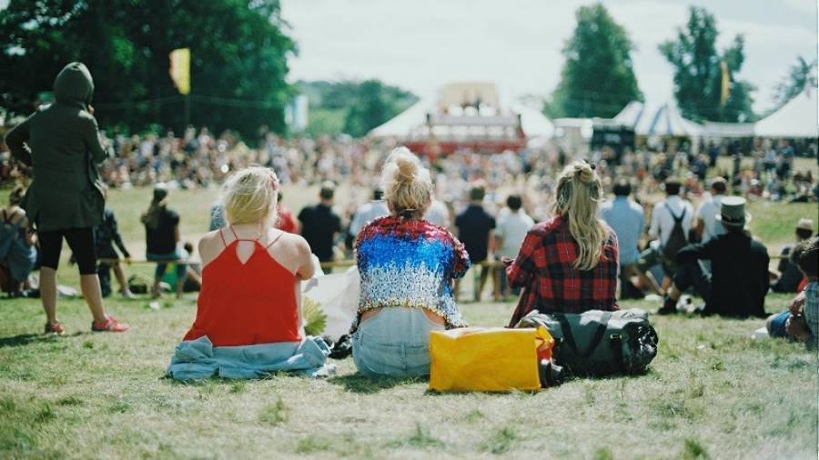 Three women sitting on grass facing towards crowds in the distance
