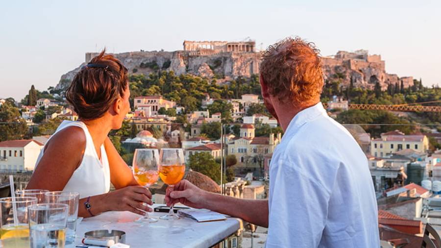 Couple dining outdoors in Athens holding wine glasses looking out to ruins
