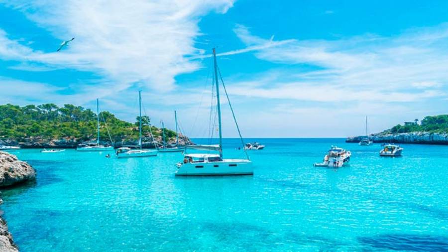 Various boats on blue Balearic waters surrounded by green rocky coast on both sides