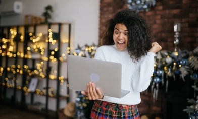 a person excitedly looking at an open laptop in a room decorated for christmas