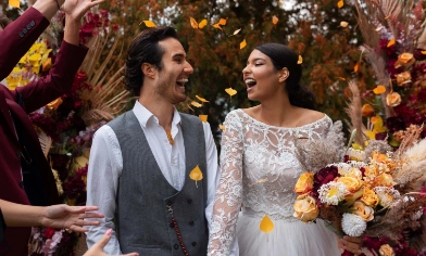 a newly married couple broadly smiling as their guests shower them with flower petals