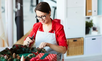 An individual crafting a holiday wreath at a table covered with festive decorations