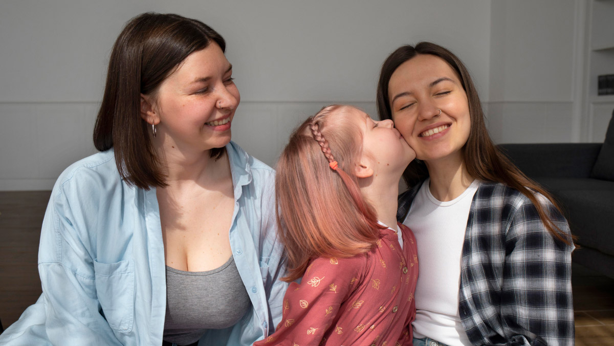 a child kissing one of her two mommies as the other looks on smiling