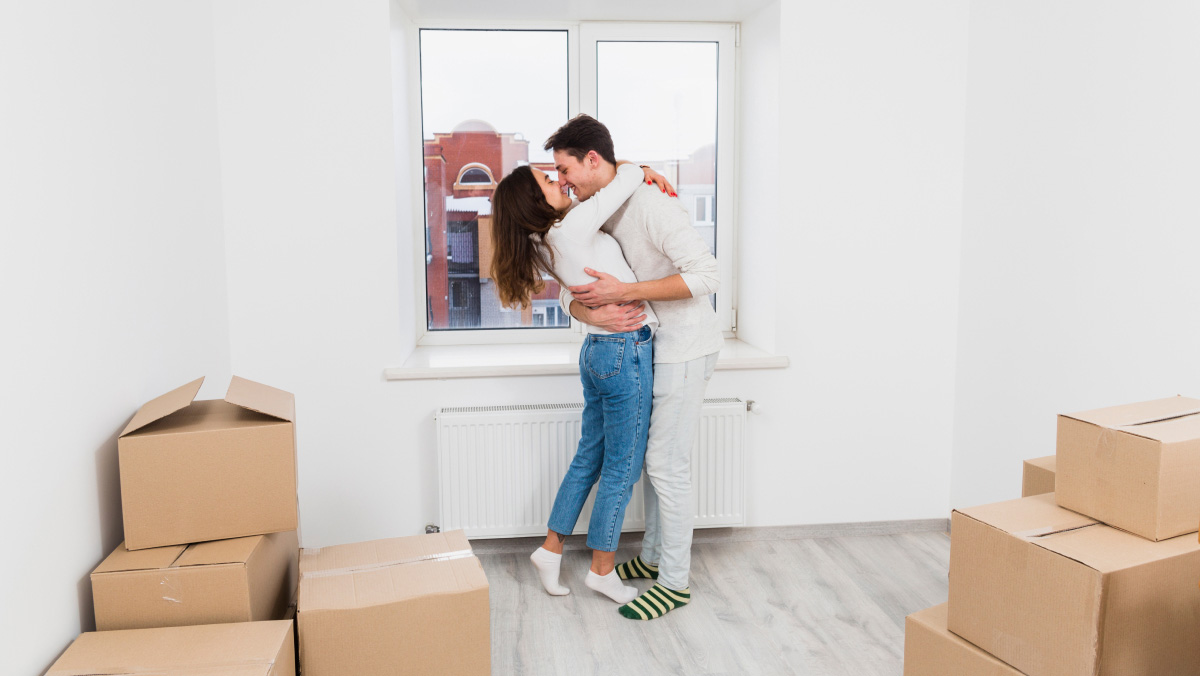 a couple kissing in front of a window surrounded by packing boxes