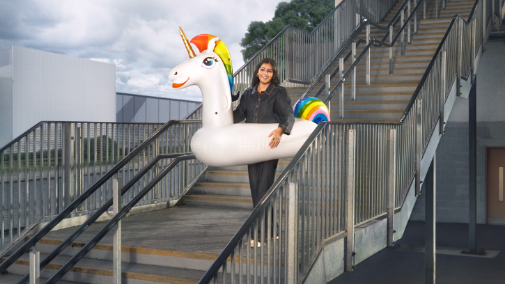 a person wearing a large rainbow unicorn pool float on a flight of stairs