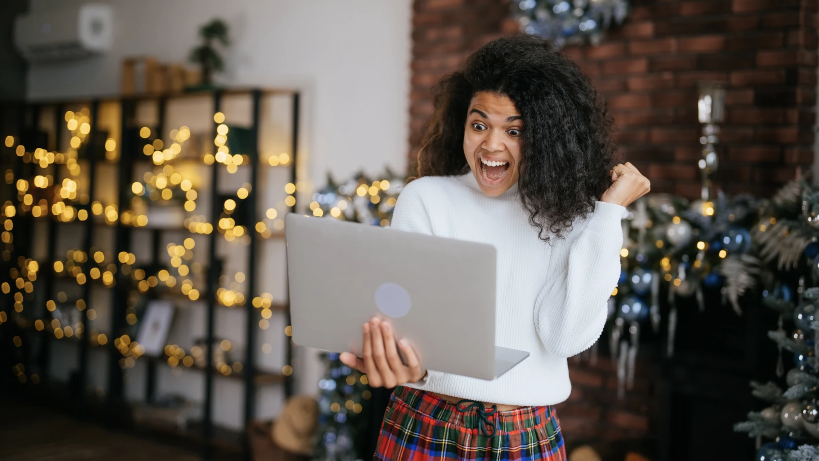 a person excitedly looking at an open laptop in a room decorated for christmas