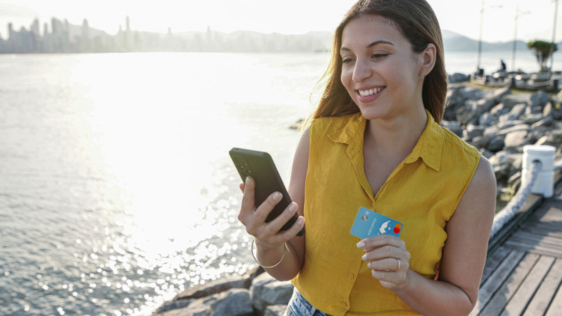 a person on a dock smiling at a smartphone while holding a credit card