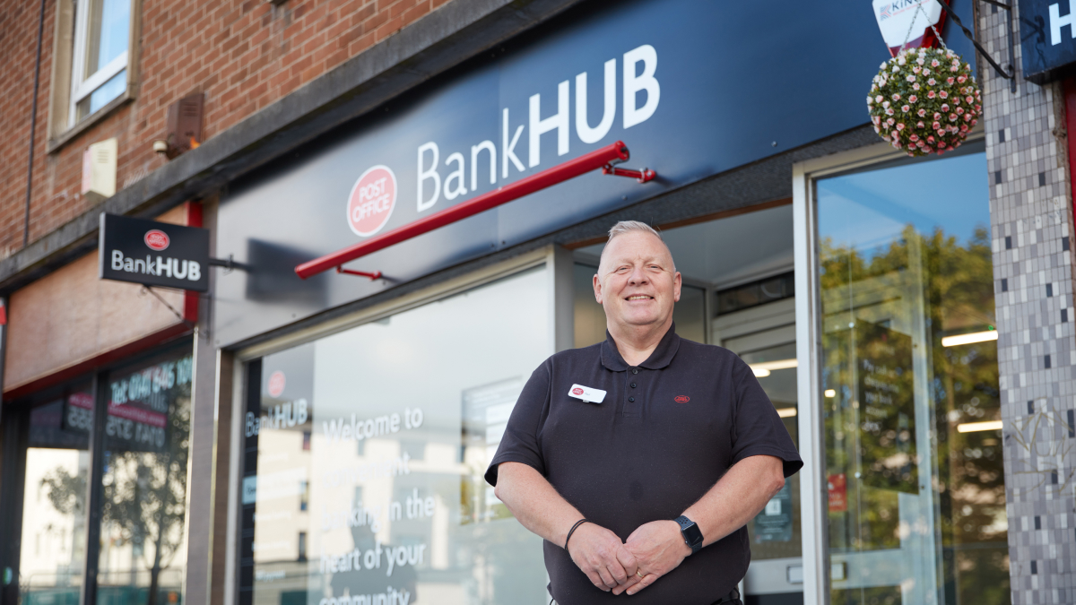 happy person standing in front of a Post Office BankHUB branded storefront