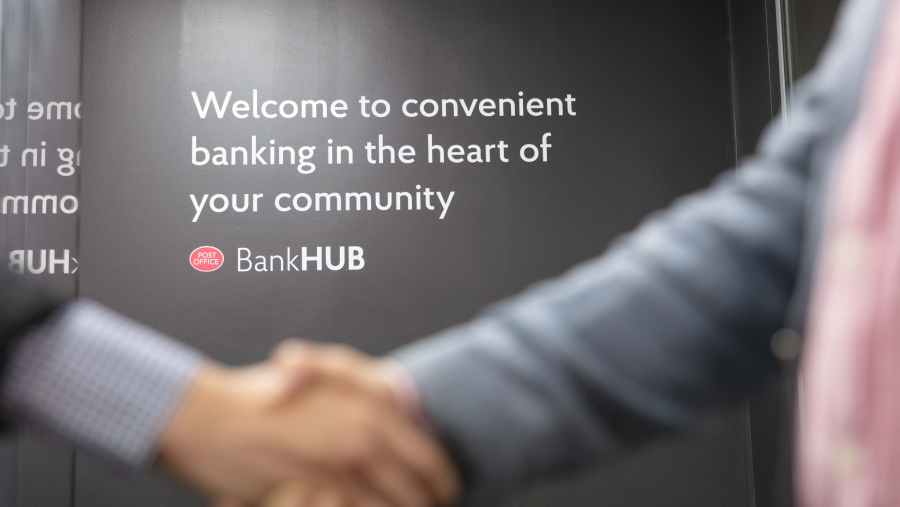 two people shaking hands in front of a Post Office Banking Hubs sign